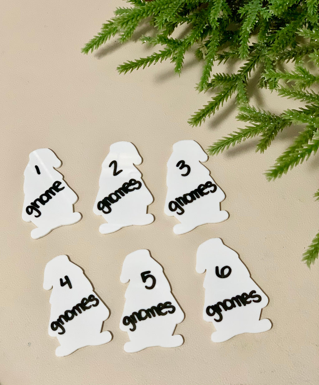 Set of six white gnome-shaped dry erase boards numbered one to six with black marker writing on beige surface with green foliage above