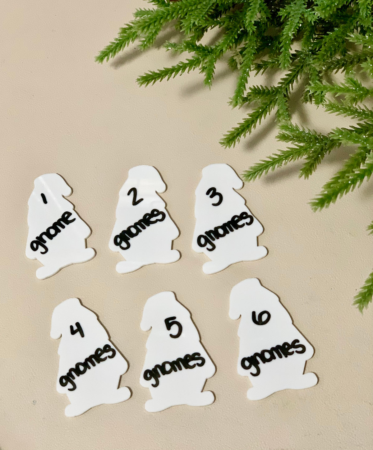 Set of six white gnome-shaped dry erase boards numbered one to six with black marker writing on beige surface with green foliage above