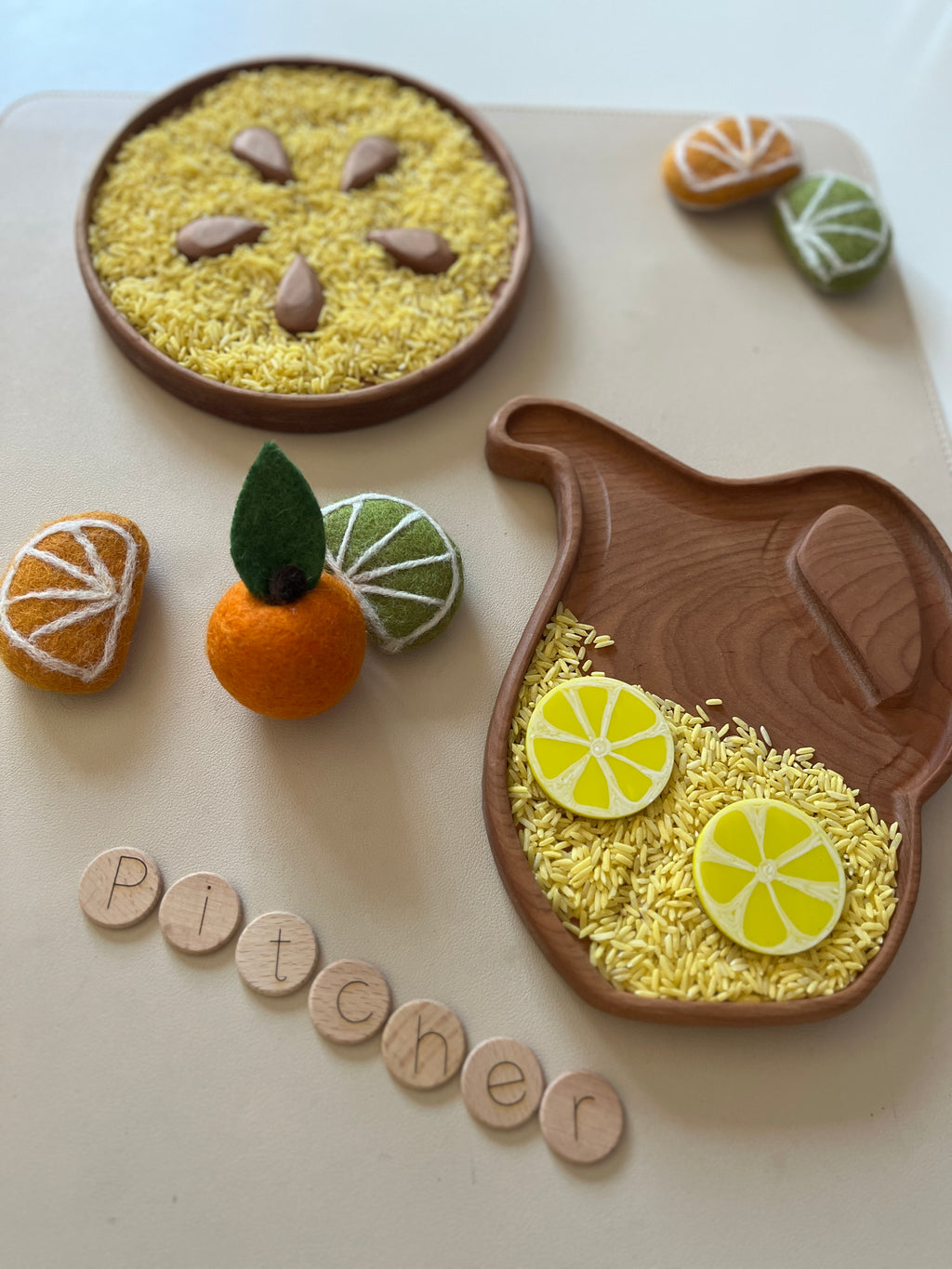 Wooden pitcher-shaped tray with yellow rice and lemon slices, felt citrus fruits, and wooden letter tiles on beige surface