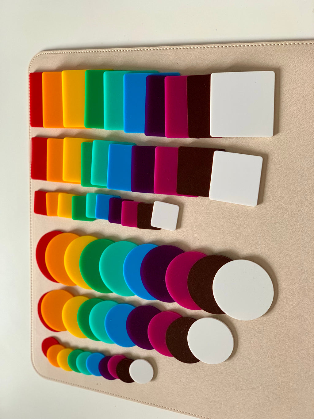 Various sizes of colorful square and circular tiles arranged on a beige surface in gradient order