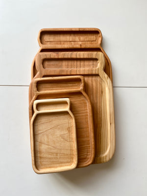 Set of four nested wooden trays shaped like jars in different natural wood tones on white surface