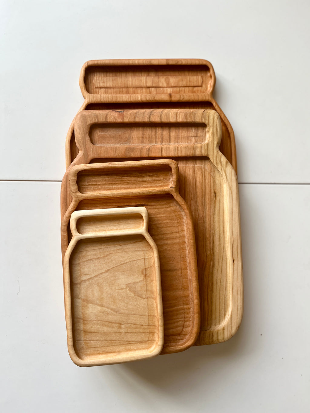 Set of four nested wooden trays shaped like jars in different natural wood tones on white surface