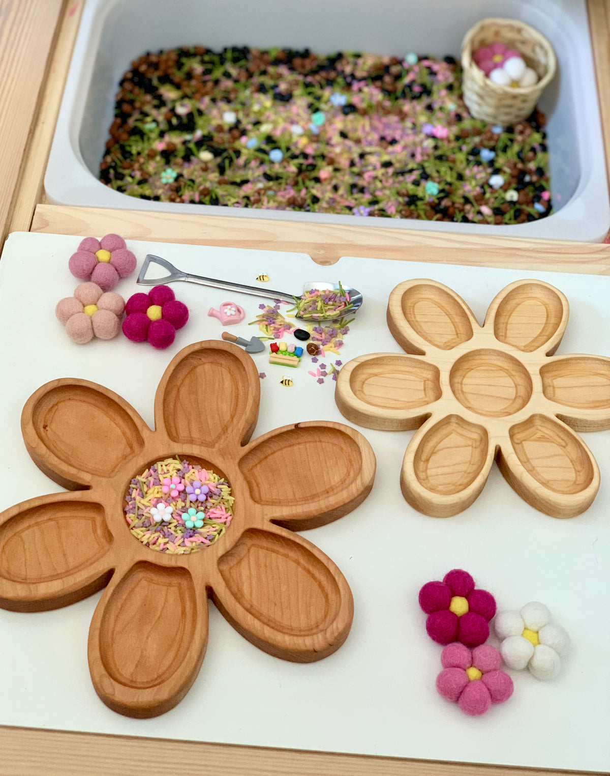 Two wooden flower-shaped trays with compartments surrounded by colorful felt flowers and floral craft supplies