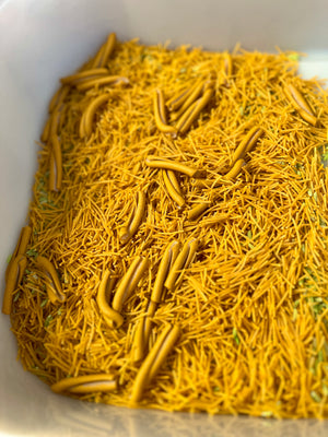 Close-up of broken yellow pasta strands mixed with uncooked tubular pasta pieces in a white container