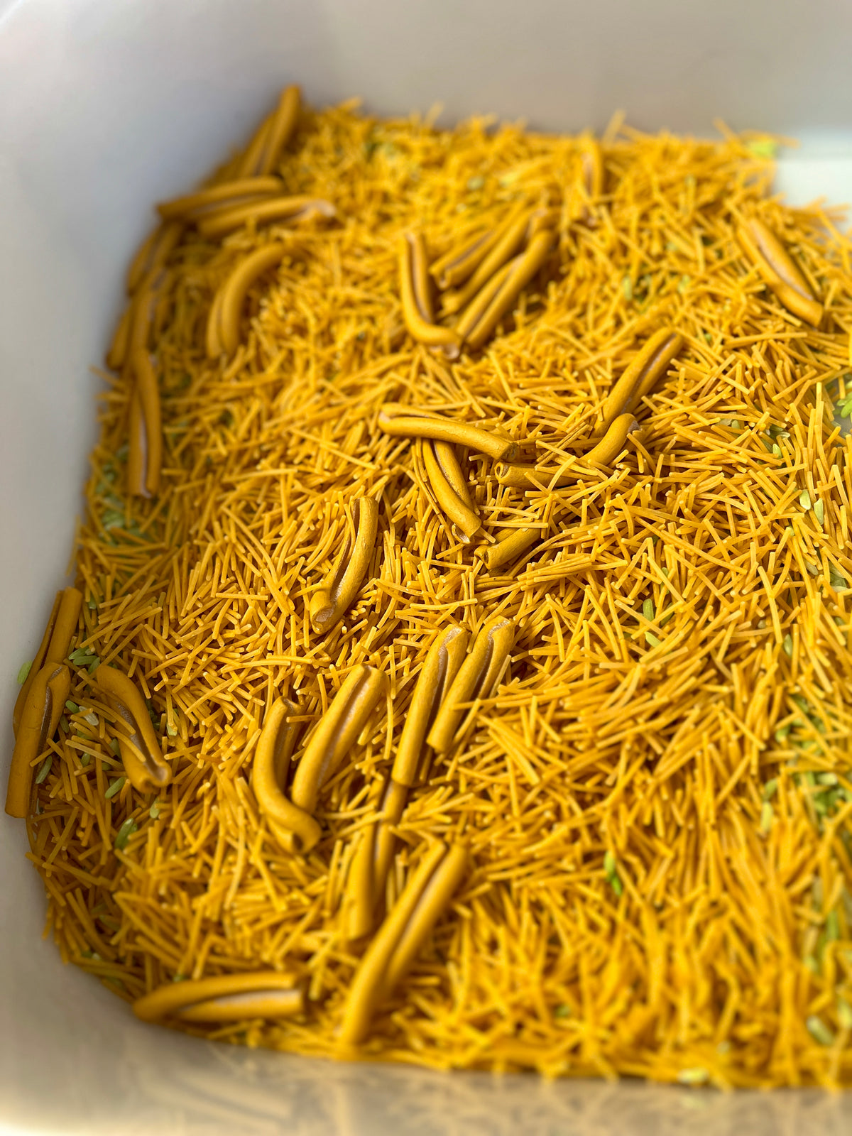 Close-up of broken yellow pasta strands mixed with uncooked tubular pasta pieces in a white container
