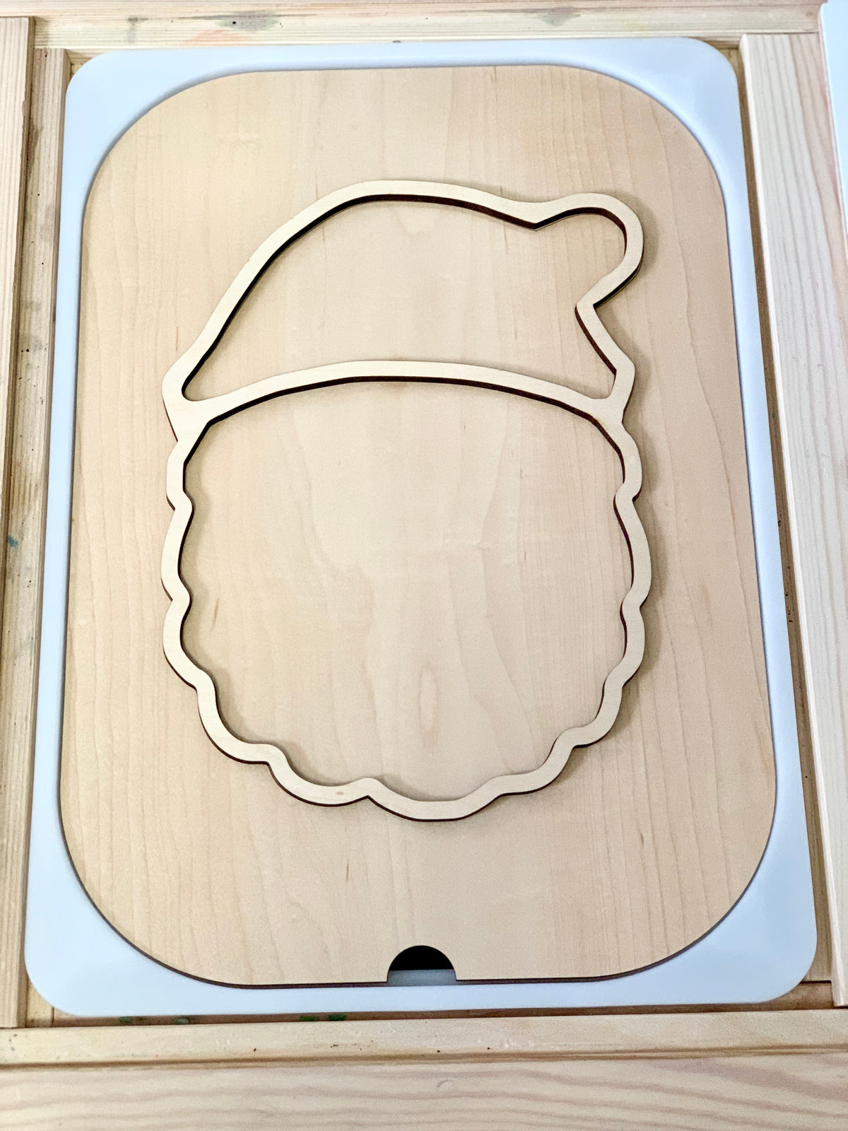 Smooth light wood puzzle insert shaped like a Santa Claus face outline with a hat and rounded features in a tray