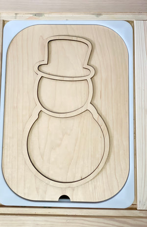 Unfinished wooden puzzle insert shaped like a snowman with a rounded top hat outline on light wood background