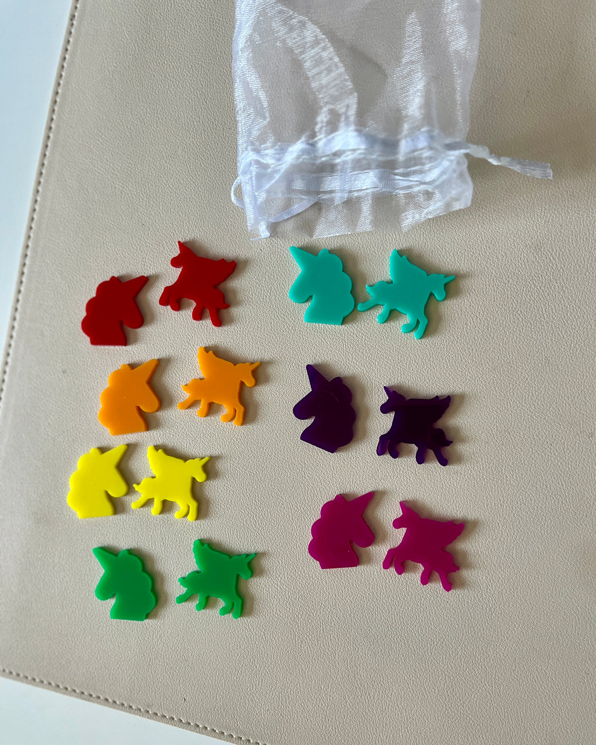 Colorful unicorn and cat-shaped game tokens arranged beside a small white mesh drawstring bag on a light surface