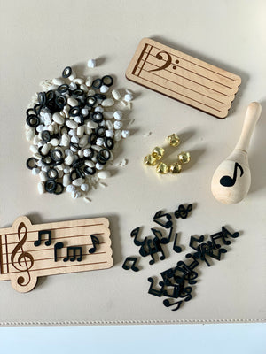 Assorted black and white musical note tokens scattered with wooden music staff plaques and a wooden maraca on a beige surface