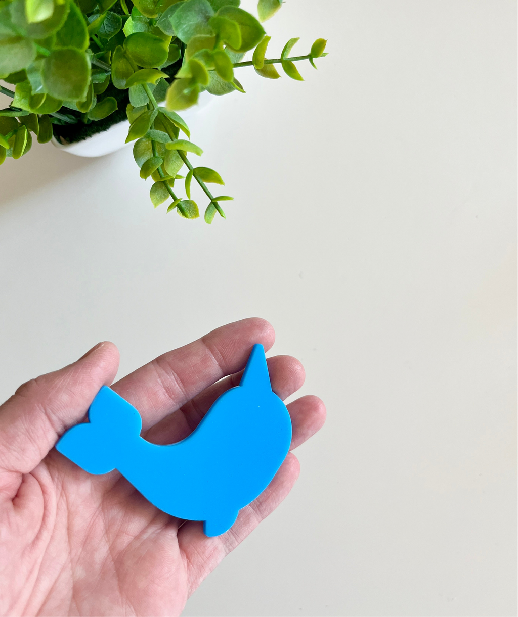 Hand holding a smooth blue whale-shaped cutout with a green leafy plant in a white pot nearby on a light surface