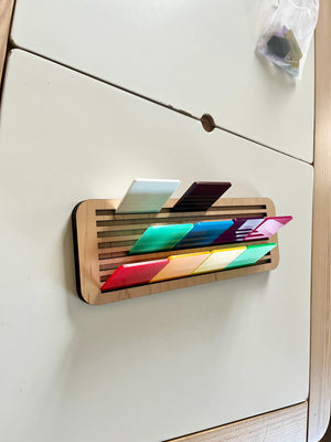 Light wooden slotted holder displaying colorful translucent rectangular tiles arranged in two rows on light surface