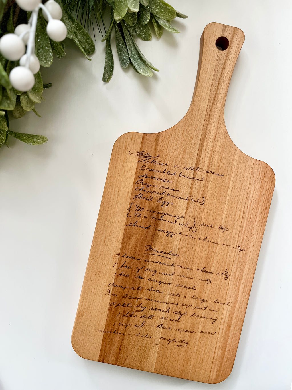 Natural wooden cutting board with laser engraved handwritten recipe on smooth wood surface with handle and hole