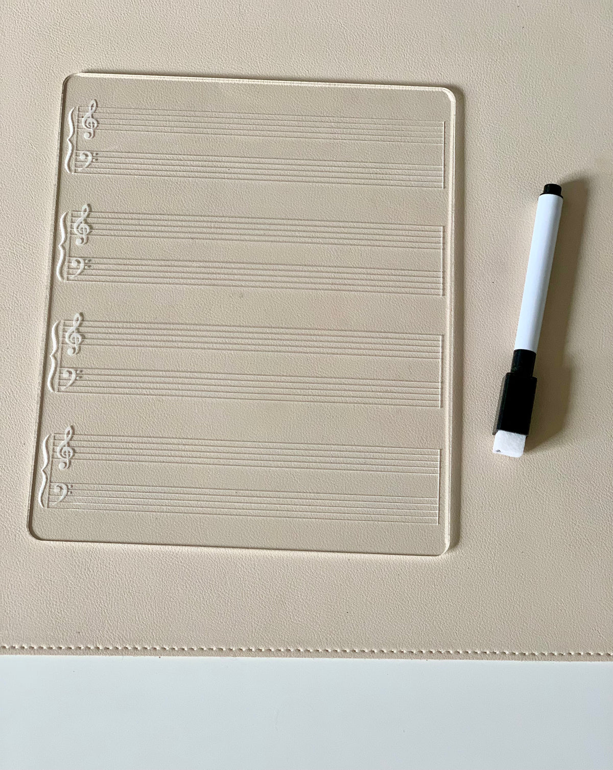 Clear music staff writing board with treble and bass clefs next to a black and white dry erase marker on beige surface