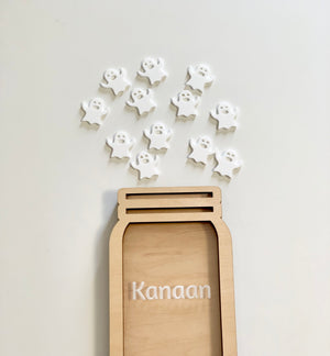 Light wooden jar-shaped frame with the name Kanaan and scattered white ghost cutouts on a plain background