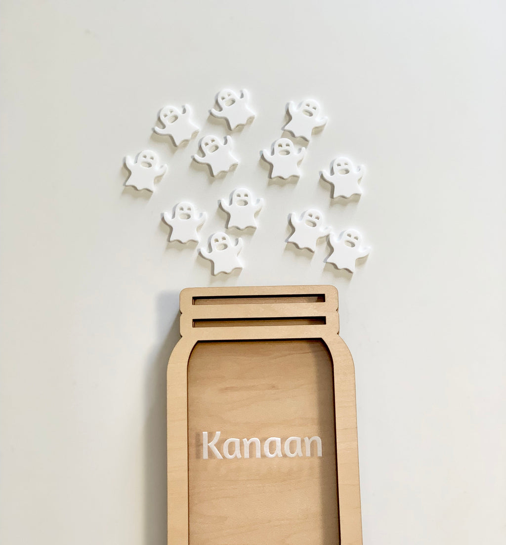 Light wooden jar-shaped frame with the name Kanaan and scattered white ghost cutouts on a plain background