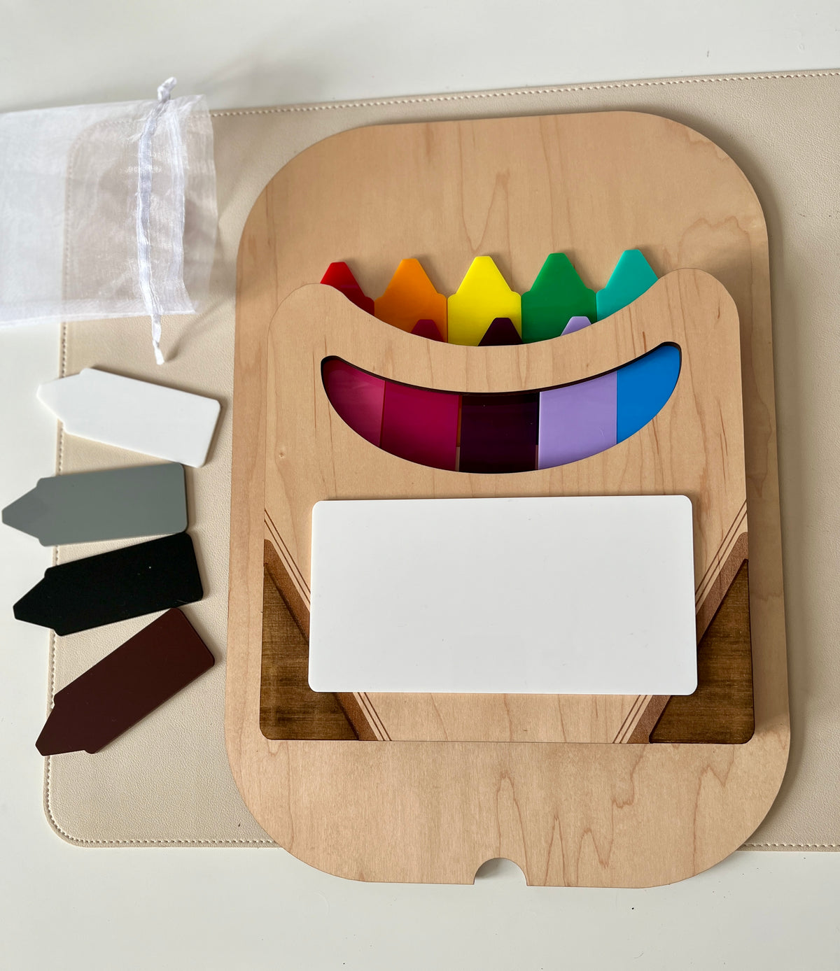 Wooden holder with colorful plastic plant markers and five blank colored tags on a beige surface next to a white mesh bag