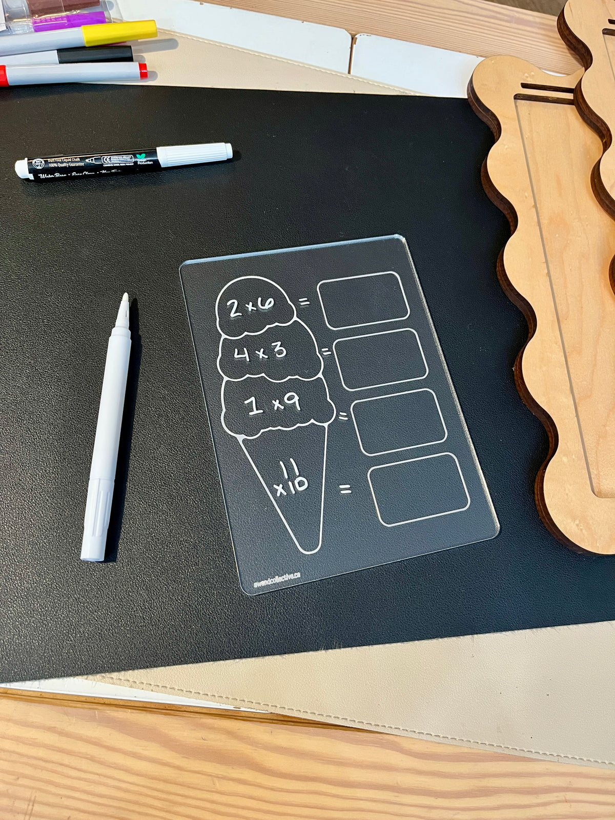 Clear acrylic math practice board shaped like ice cream with multiplication problems and white marker on black surface