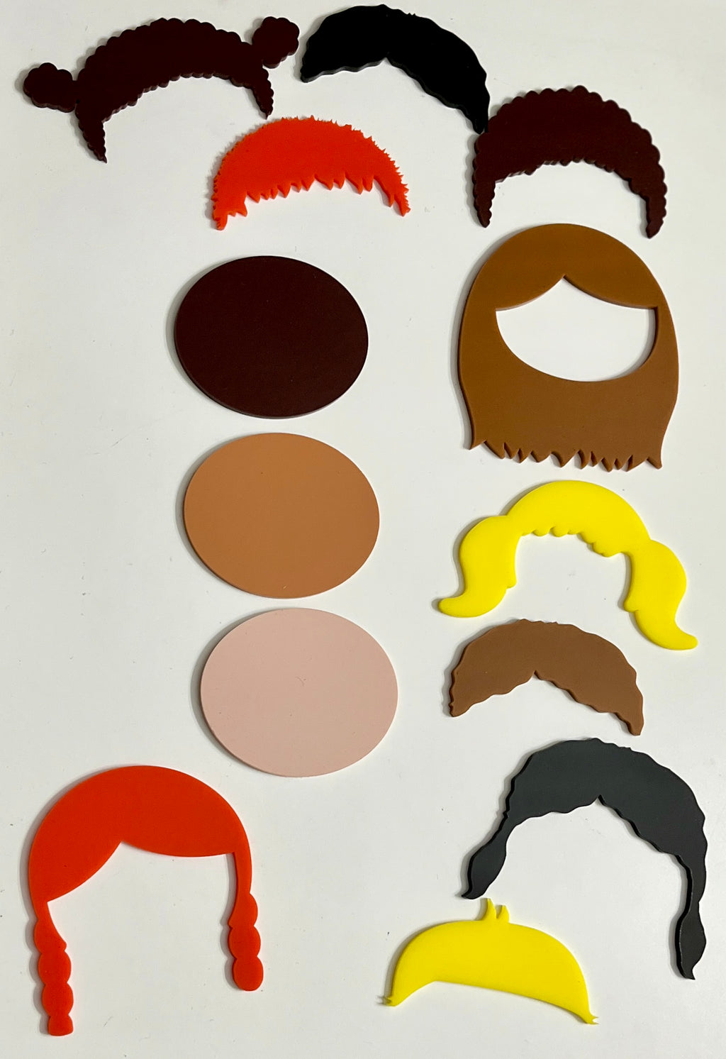 Colorful flat face cutouts in various skin tones with matching hair shapes in different styles arranged on a white background
