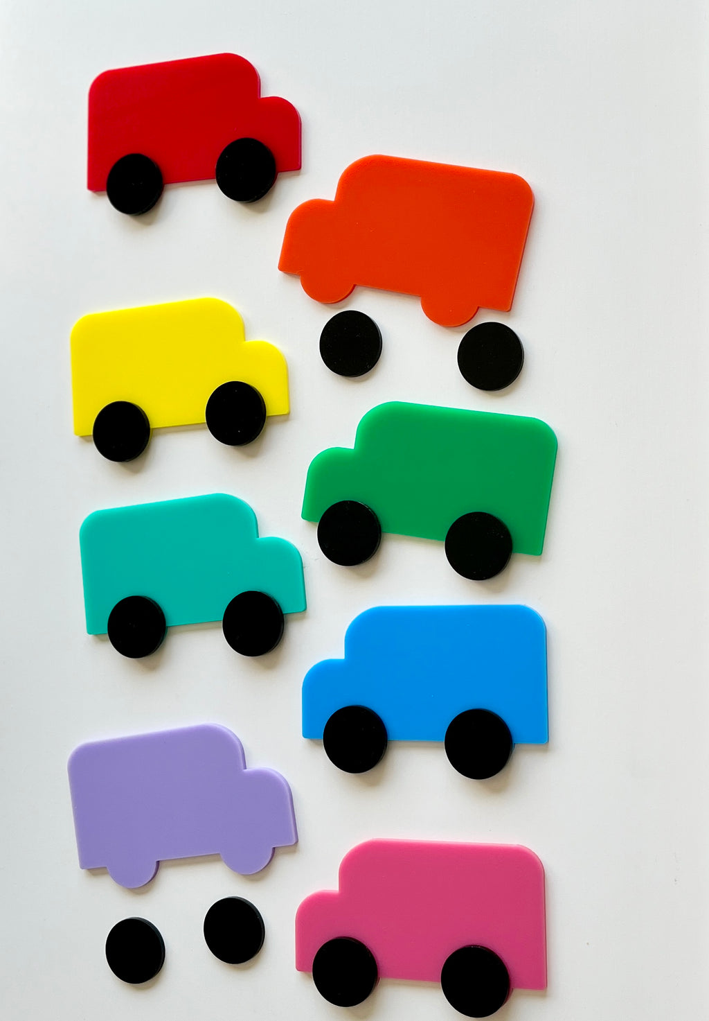 Eight colorful abstract toy trucks in red, orange, yellow, green, teal, blue, purple, and pink with separate black wheels on white background