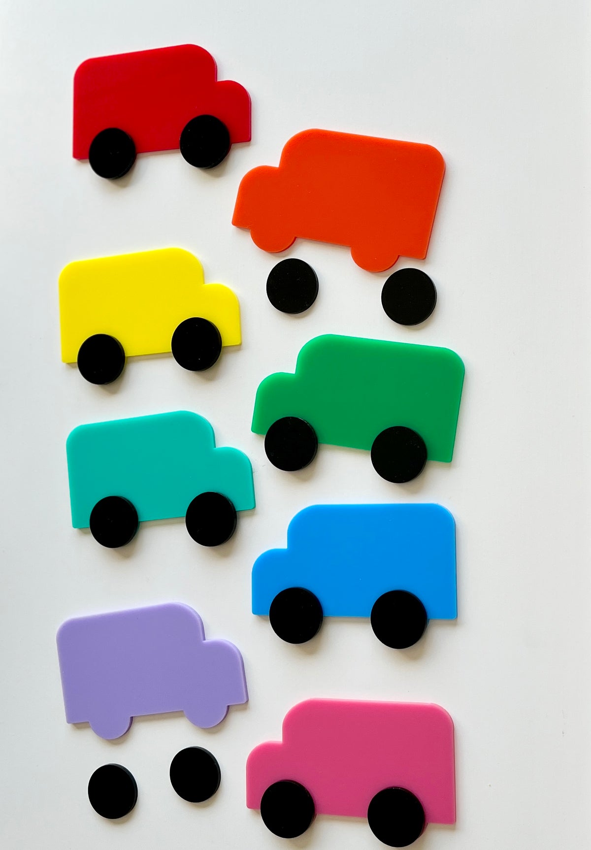 Eight colorful abstract toy trucks in red, orange, yellow, green, teal, blue, purple, and pink with separate black wheels on white background