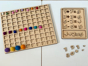 Laser cut hundred sorting board sensory tray with numbered slots and colorful felt balls alongside wooden math puzzle pieces on white surface