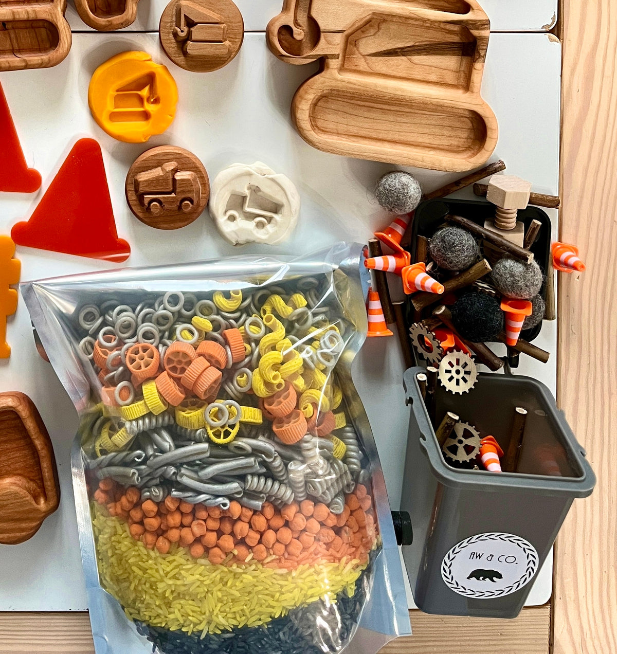 Clear bag filled with colorful plastic nuts, bolts, and washers next to wooden tools and small toy traffic cones