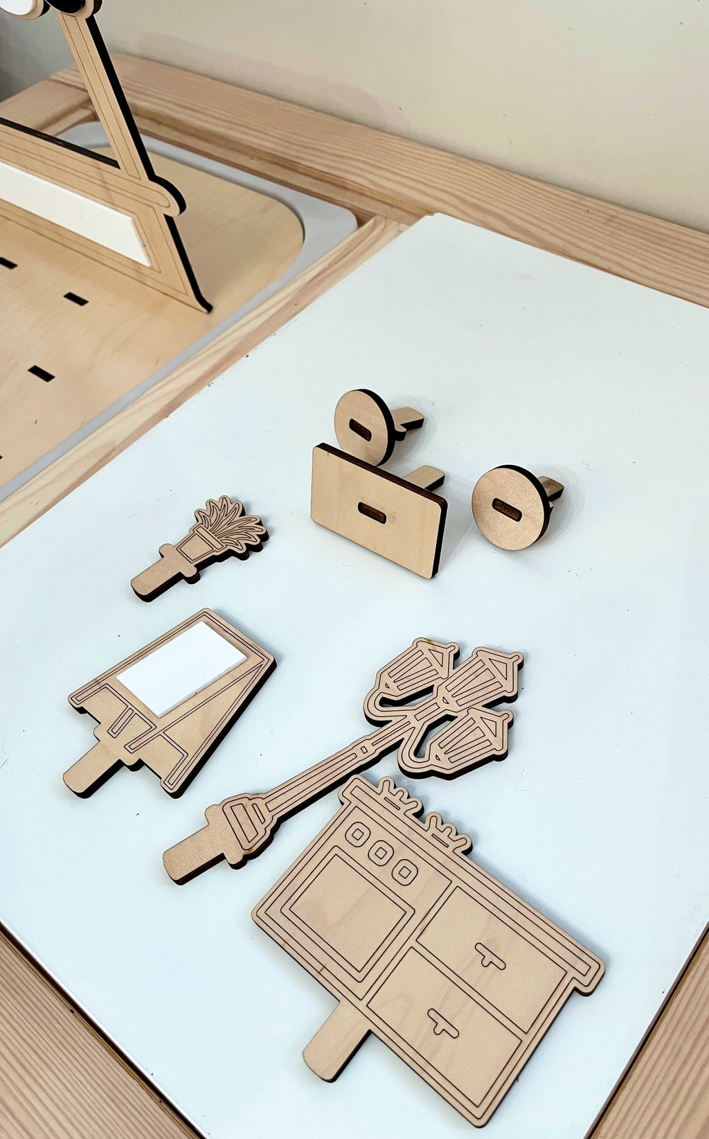 Laser-cut wooden play pieces including a stove, lamp post, street sign, plant, and two circular connectors on a white surface