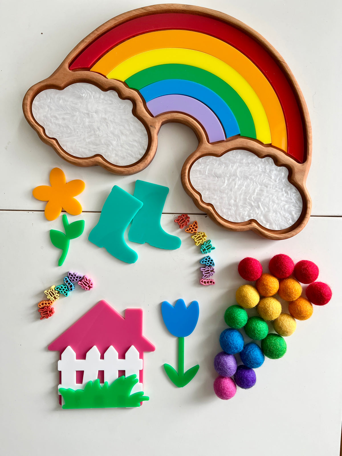 Wooden rainbow tray with colorful arch pieces, textured white cloud sections, and assorted colorful shapes on white surface