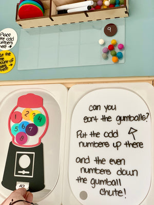 Hands sorting colorful numbered circles on a paper gumball machine with odd-even number sorting instructions