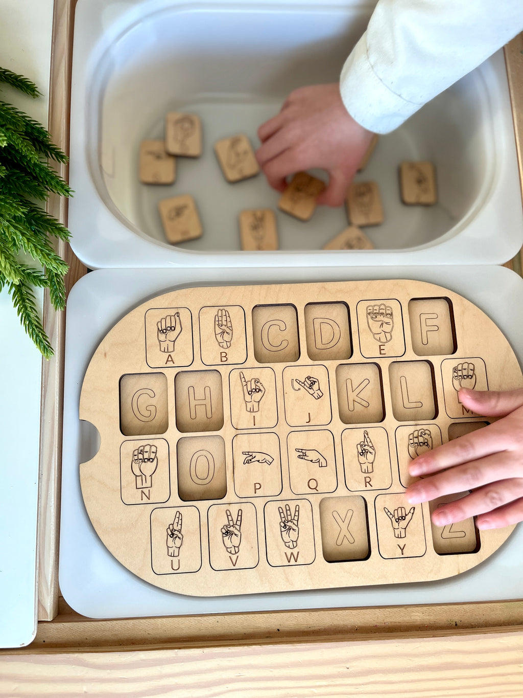 Child placing wooden ASL alphabet puzzle pieces into maple plywood Flisat table top insert on white bin tray