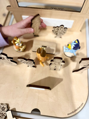 Child’s hand placing wooden and plastic animal figures on a natural wood playboard with engraved details