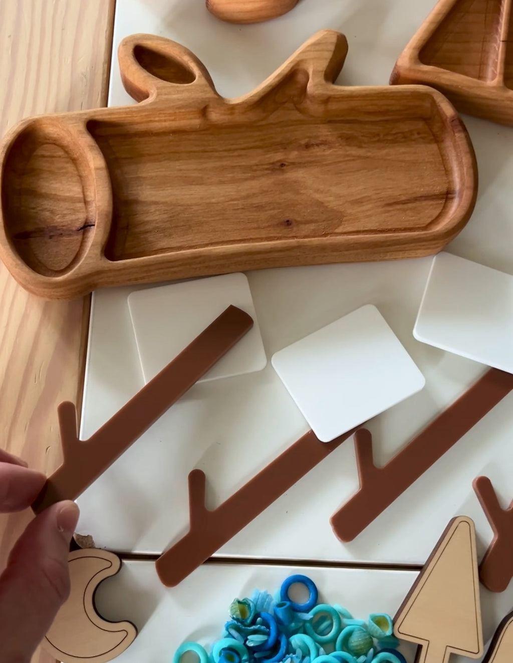 Carved wooden tray shaped like a log with brown twig cutouts, white cards, and blue spiral shapes on table