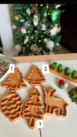 Wooden trays shaped like pinecone, various trees, and a reindeer arranged on table with decorated Christmas tree background