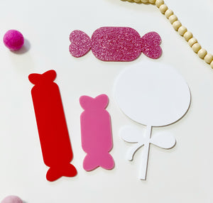 Four little dry erasable candy-shaped boards in red, pink, glittery pink, and white with bead and pom accents on white surface