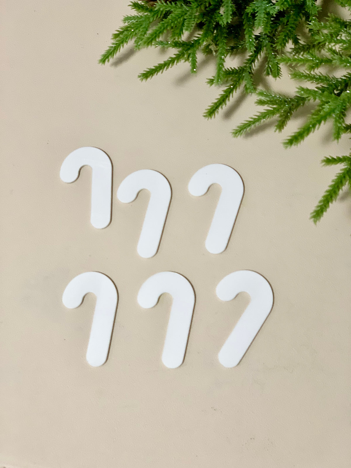 Set of six white candy cane-shaped dry erase boards on beige surface with green pine branches above