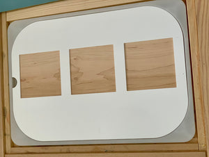 White board with three rectangular wooden shapes of varying sizes arranged horizontally on a wooden surface