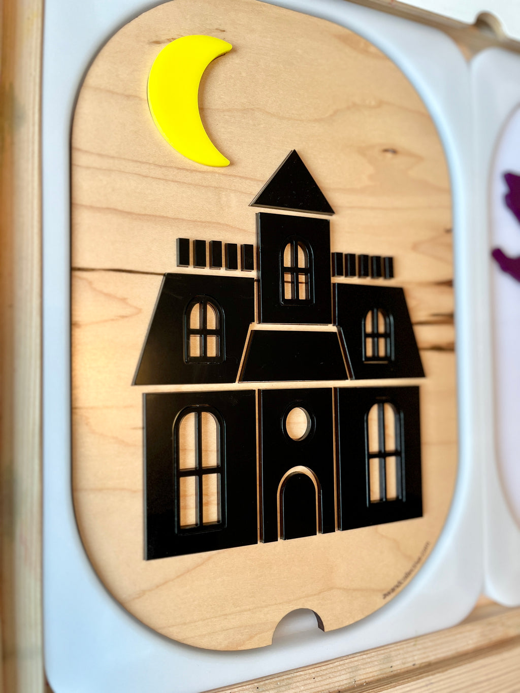 Black silhouette of a haunted house with arched windows and a yellow crescent moon on a wooden base