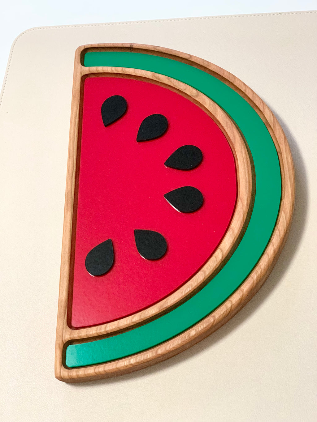 Wooden sensory tray shaped like a watermelon slice with red and green painted sections and six black seeds