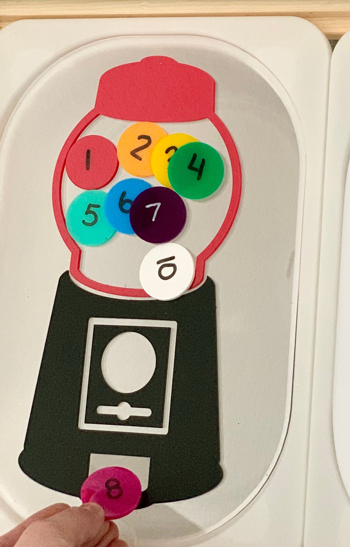 Paper craft shaped like a gumball machine filled with colorful numbered circles on a white surface