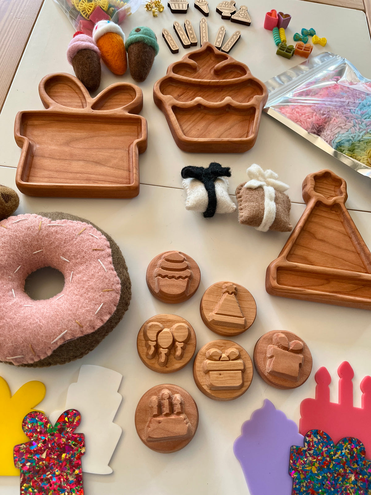 Wooden trays shaped like cupcake, gift box, party hat, carved stamps, felt donuts, and colorful crafting supplies on table
