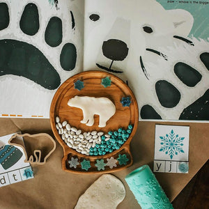 Round wooden sensory tray shaped like a snow globe with polar bear, white and blue stones, and snowflake decorations