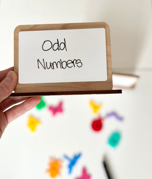 Hand holding a small whiteboard with 'Odd Numbers' text against a colorful background
