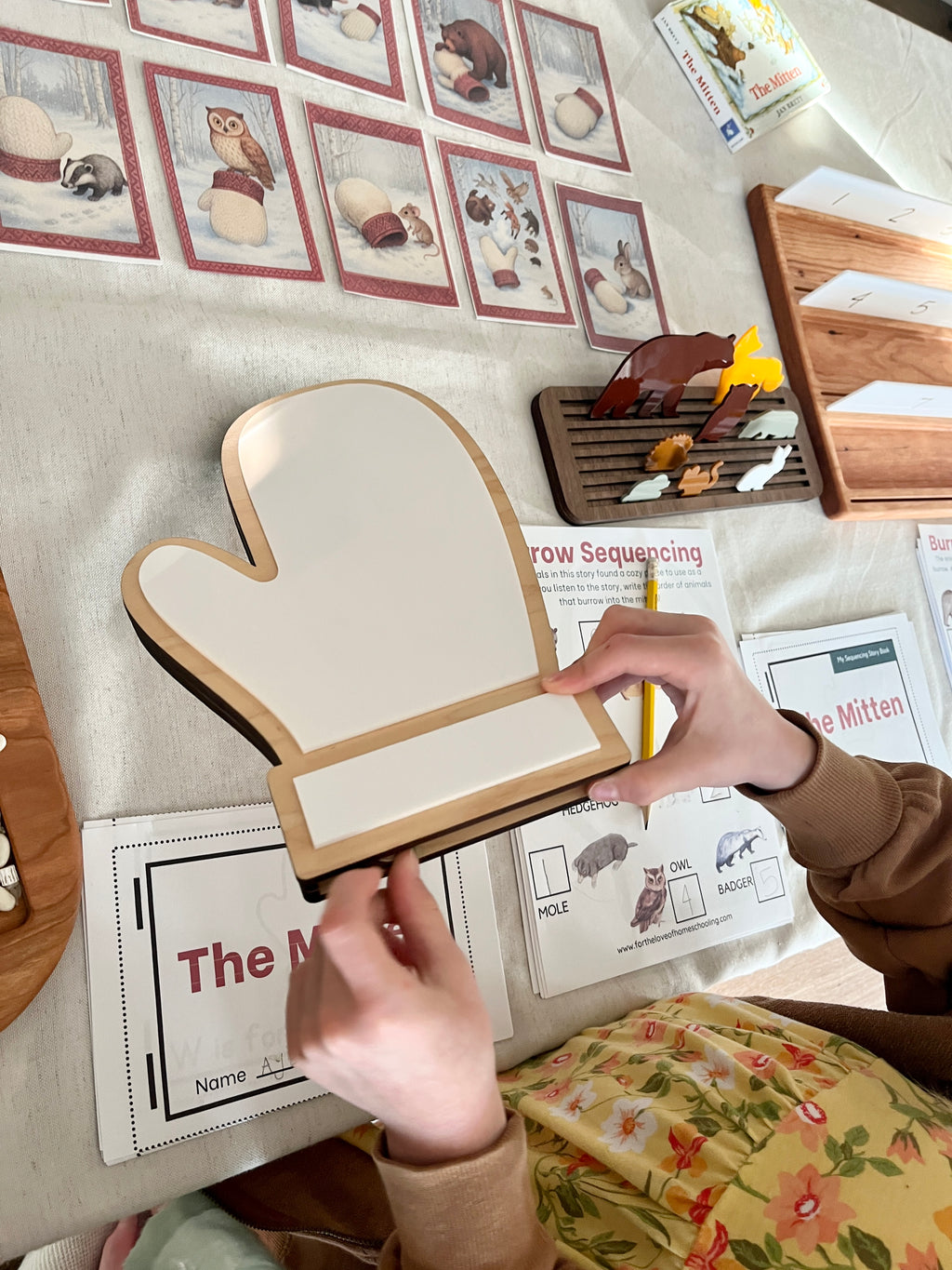 The Mitten Wooden Animals and/or Little Dry Erasables with Mitten Interactive Learning Set showing a child engaging with a wooden mitten-shaped dry-erase board surrounded by educational cards and wooden animal figures, handcrafted homeschool education resources.