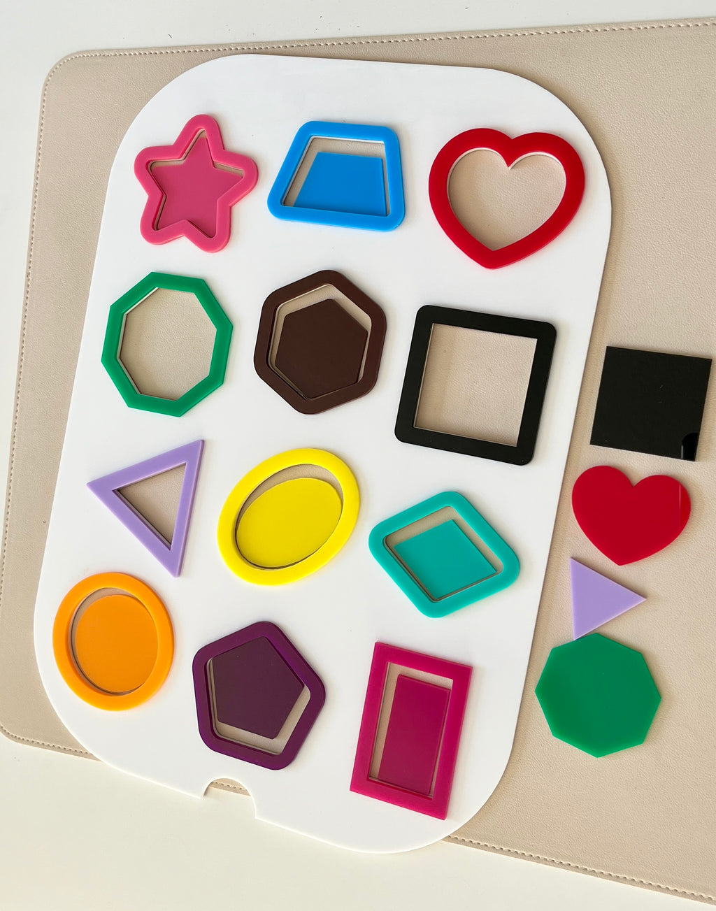 Assorted colorful plastic shape outlines arranged on a white board with three solid shapes on the side