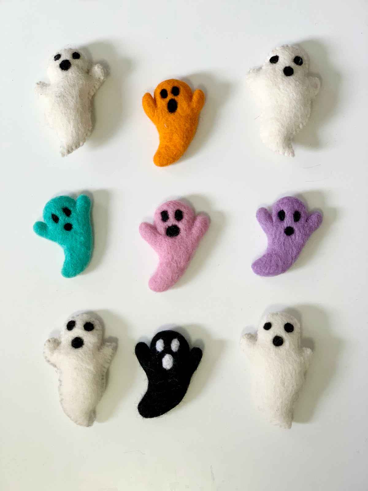 Nine handmade felt ghost figures in white, orange, teal, pink, purple, and black on white background