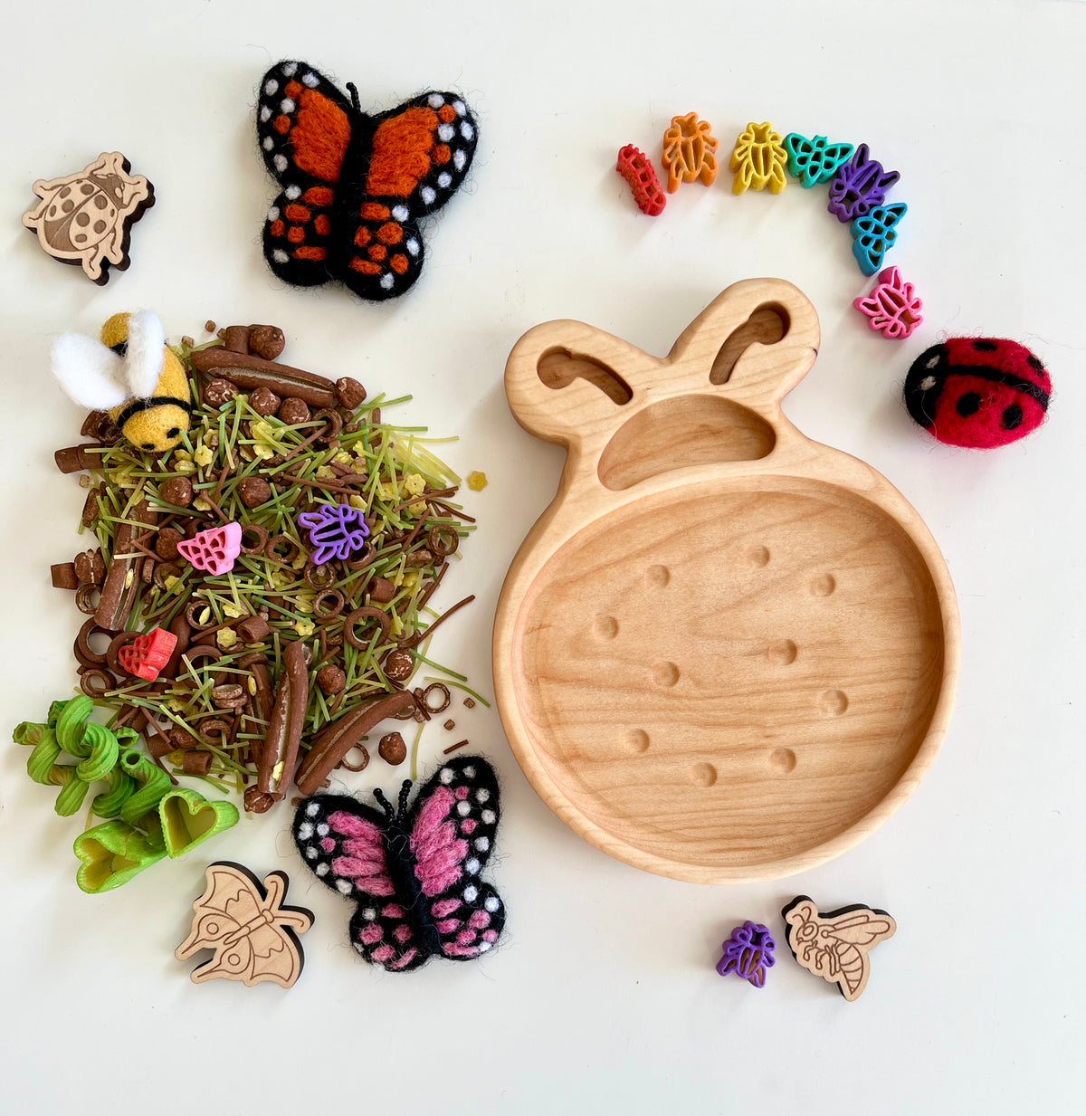 Wooden bee-shaped tray with colorful insect-themed beads, felt butterflies, wooden insect cutouts, and natural craft materials on white background