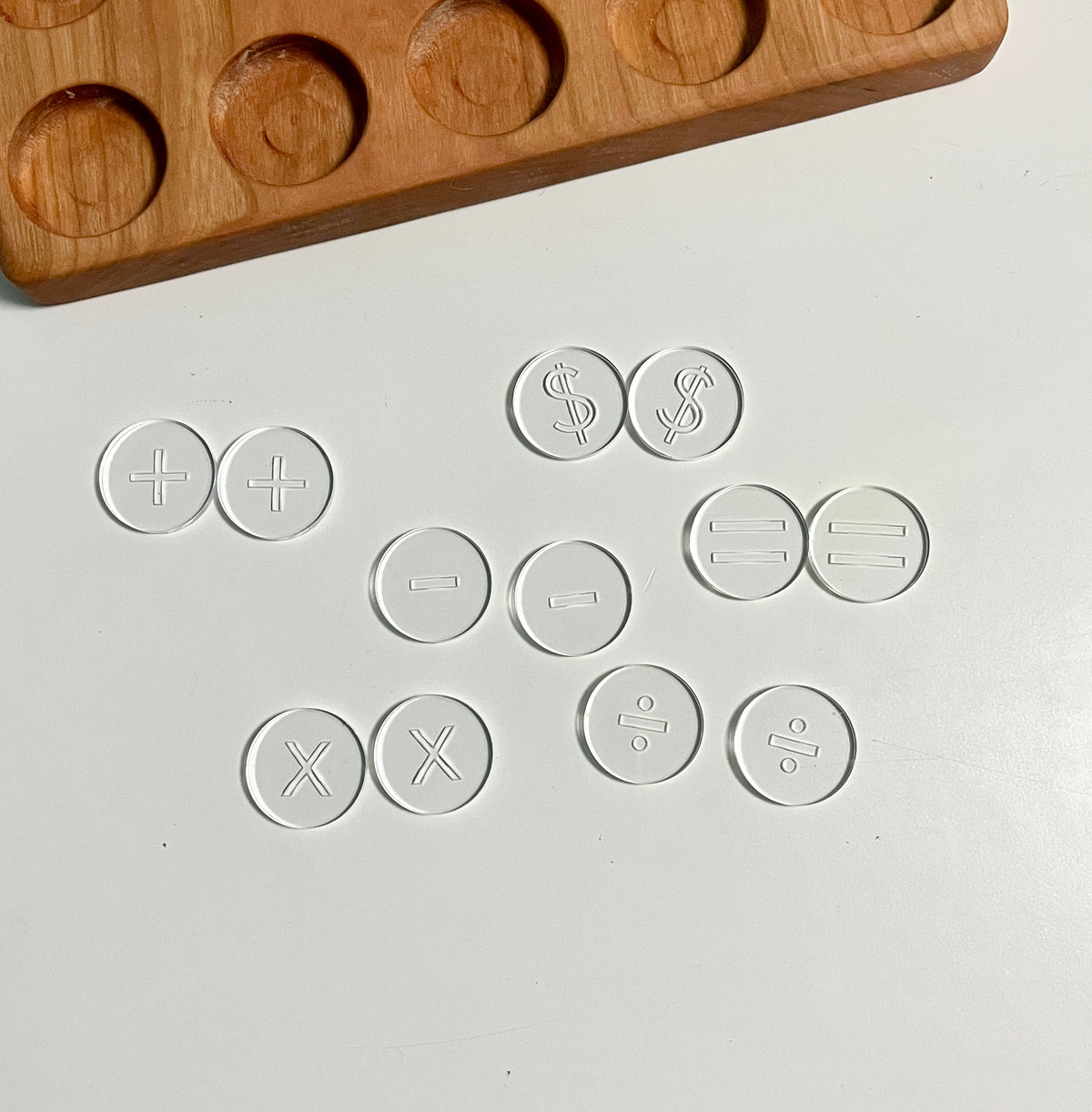 Mini Wood or Clear Acrylic Math Symbol Discs featuring translucent discs with embossed math symbols arranged near a wooden tray, handcrafted homeschool educational resources for tactile learning.