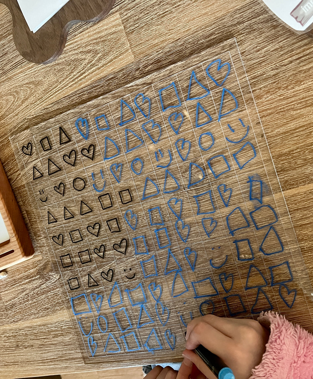 Dry Erasable Blank Open Ended 100 Frame Hundred Board on wooden surface with blue and black hand-drawn shapes including hearts, squares, triangles, and smiley faces, handcrafted homeschool education resources.