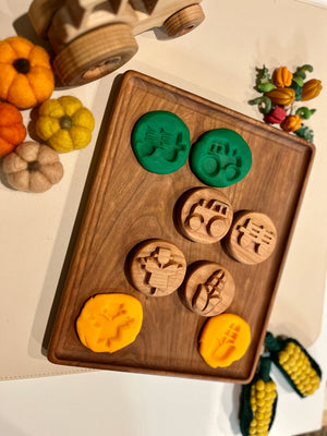 Wooden playdough stamps with green and yellow dough impressions on a wooden tray surrounded by felt pumpkins and corn decorations