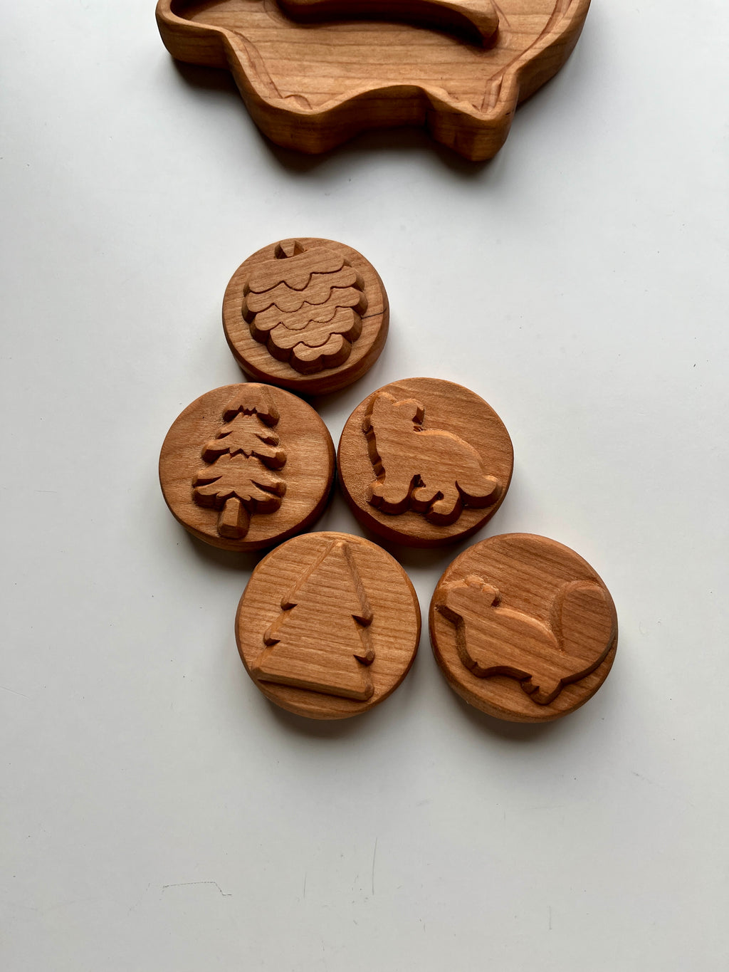 Set of five round wooden tokens engraved with forest-themed shapes on a plain white surface